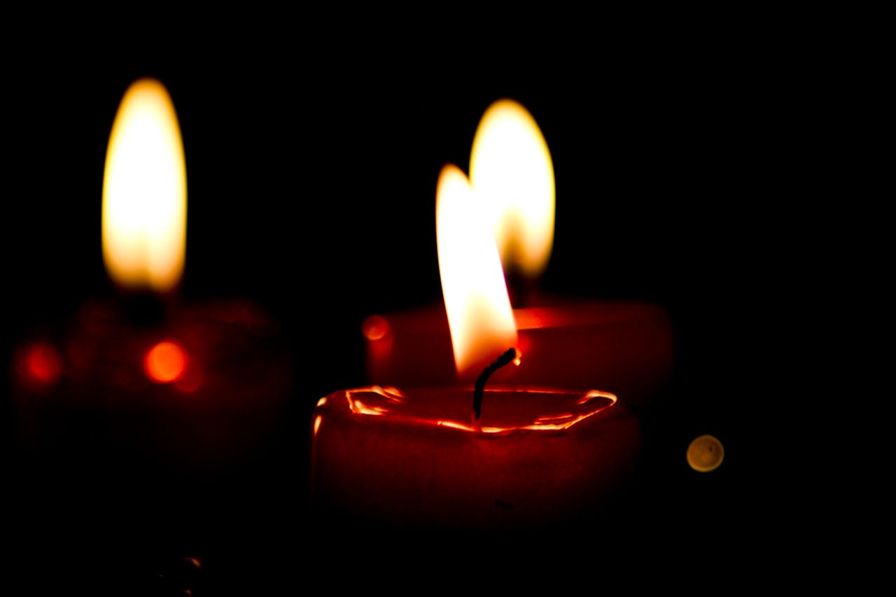 Close-up of three candles burning on a dark background, creating a warm glow.